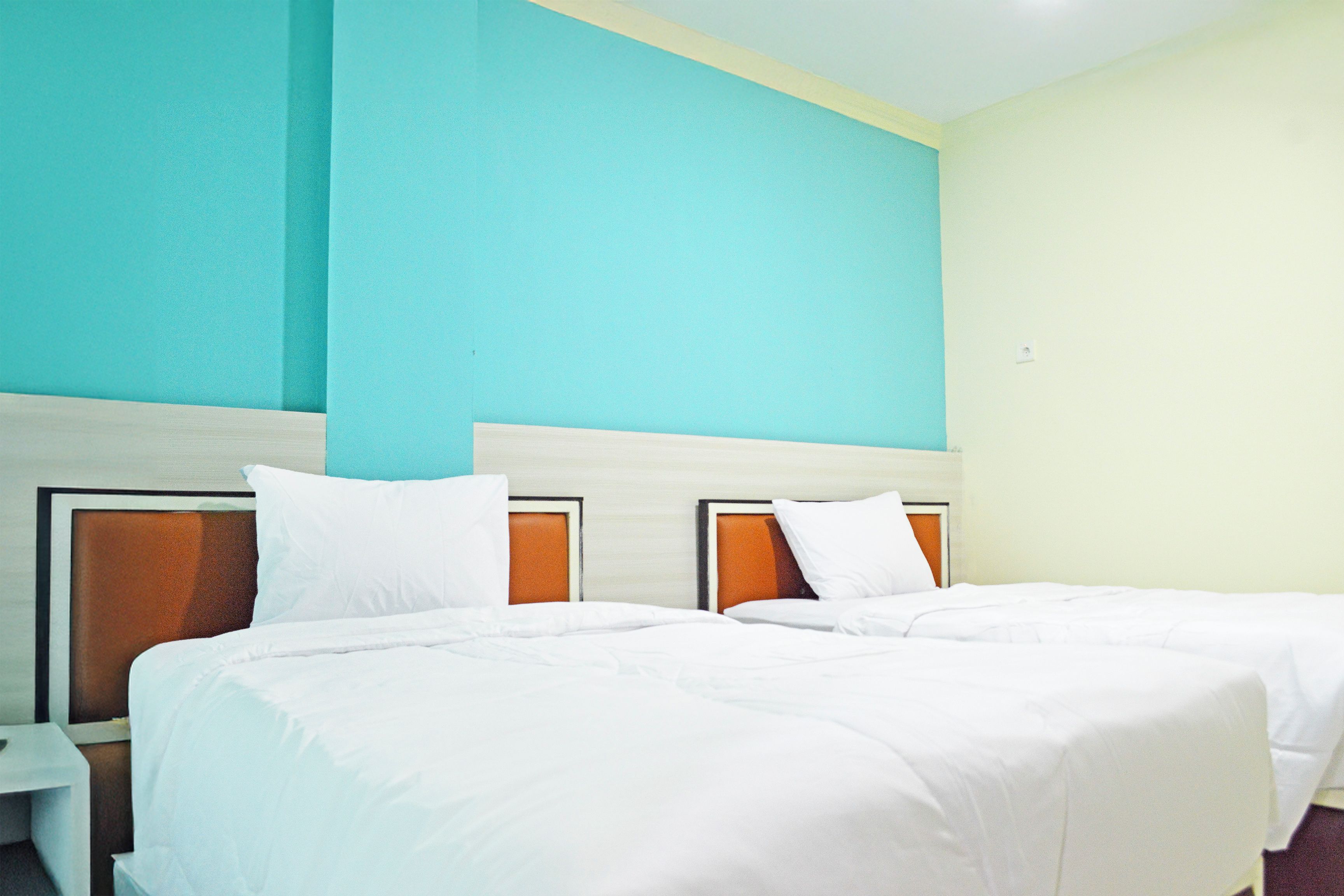 Een hotelkamer met twee bedden, een nachtkastje en een lichtgekleurde muur.