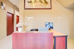 A reception desk with a sign reading "RECEPTIONIS," a laptop, a monitor, and a framed picture of horses on the wall. - Collection O Padang C Center Near Transmart Padang (Padang)