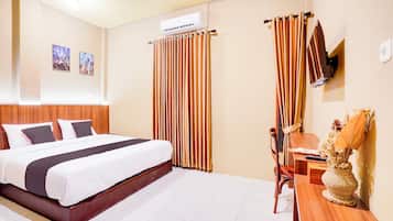 A hotel room with a large bed, a wooden headboard, a desk with a chair, and a wall-mounted TV.