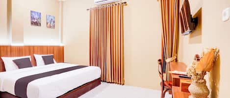 A hotel room with a large bed, a wooden headboard, a desk with a chair, and a wall-mounted TV.