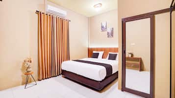 A hotel room with a bed, a mirror, a small table with a vase, and a window with curtains.