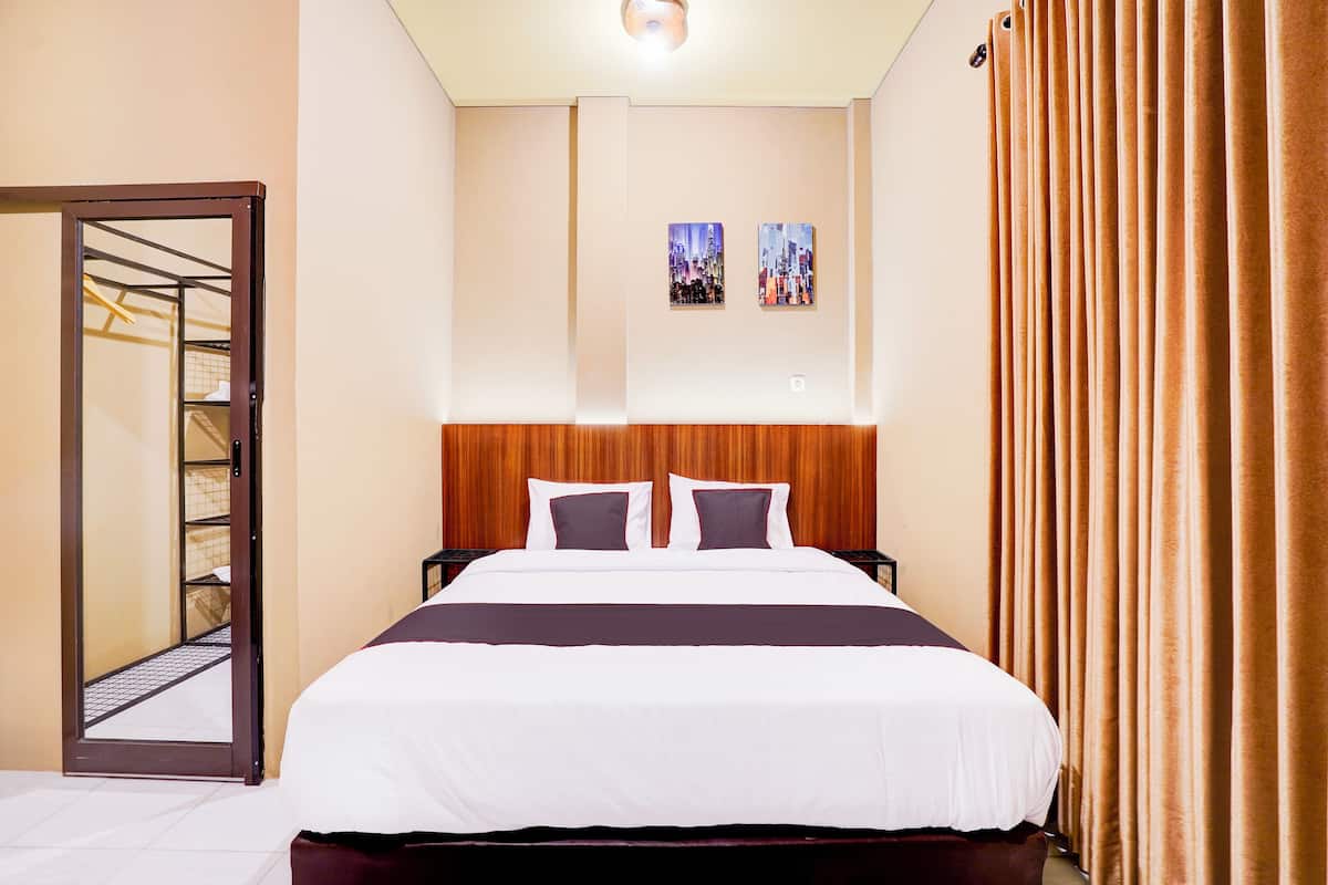 Quarto de hotel com uma cama grande, cabeceira de madeira, duas imagens penduradas na parede e vista para a paisagem urbana pela janela.