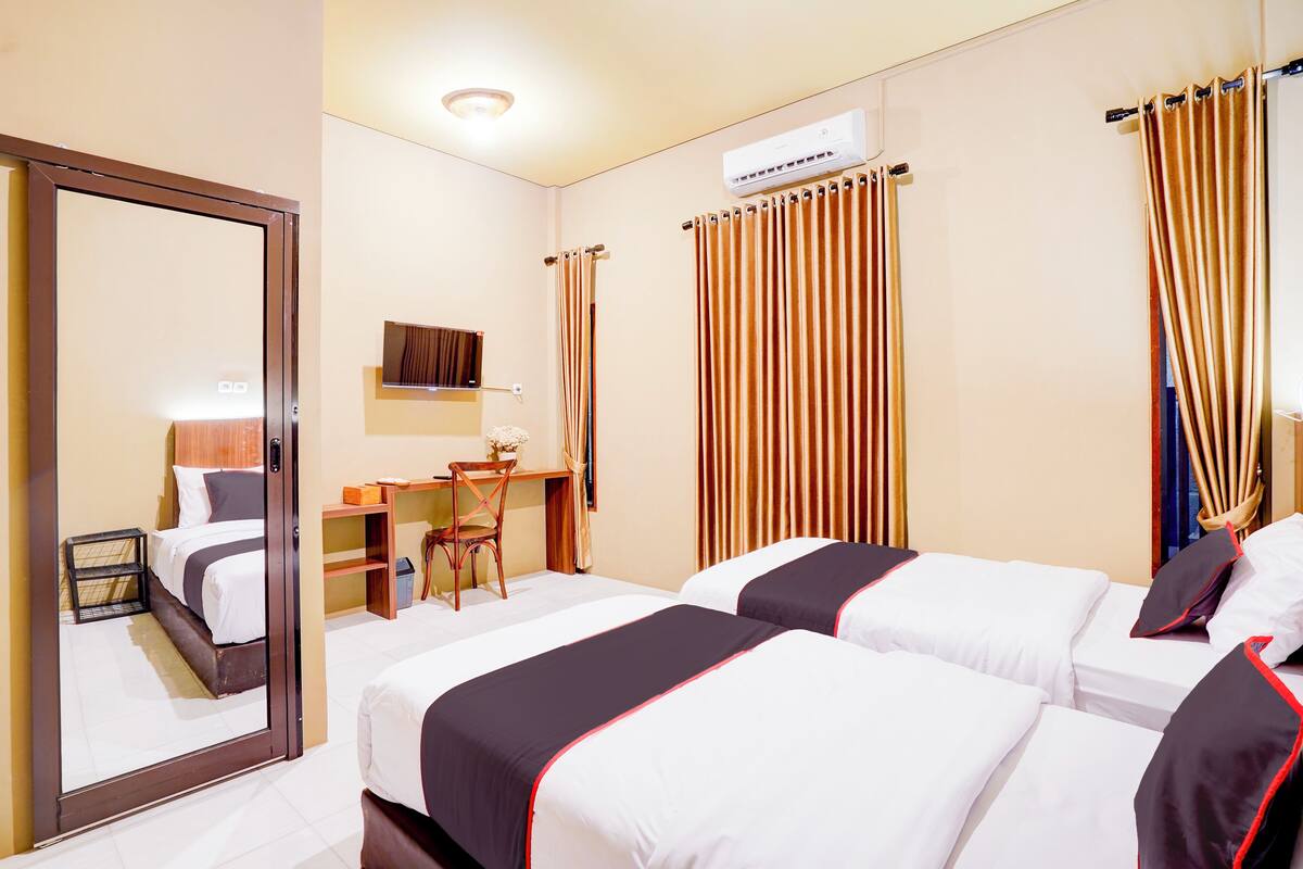 Quarto de hotel com duas camas, uma escrivaninha, uma cadeira e um espelho.