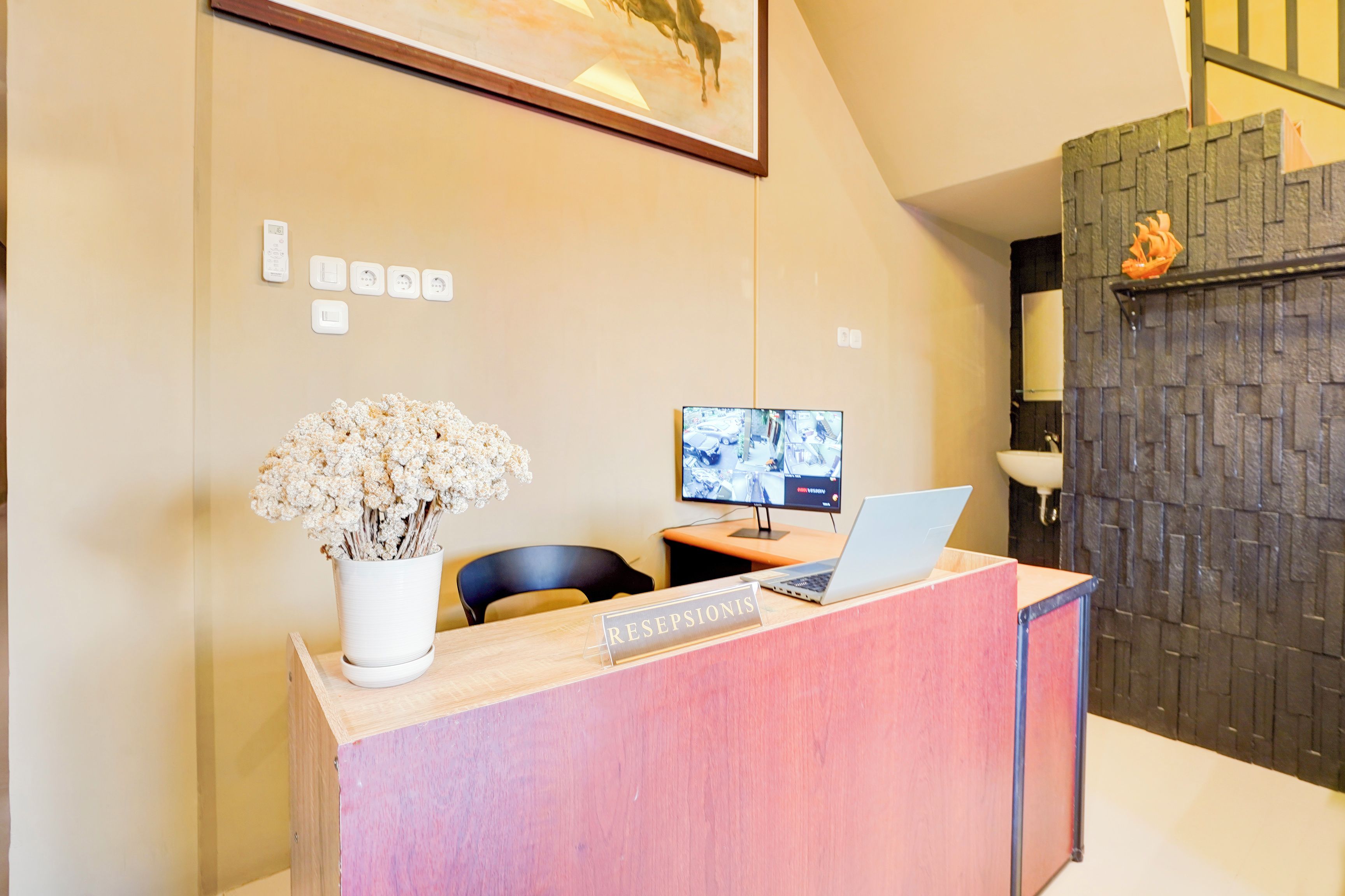 A reception desk with a laptop, a framed picture, and a vase of dried flowers.