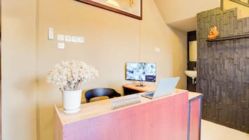A reception desk with a laptop, a framed picture, and a vase of dried flowers.