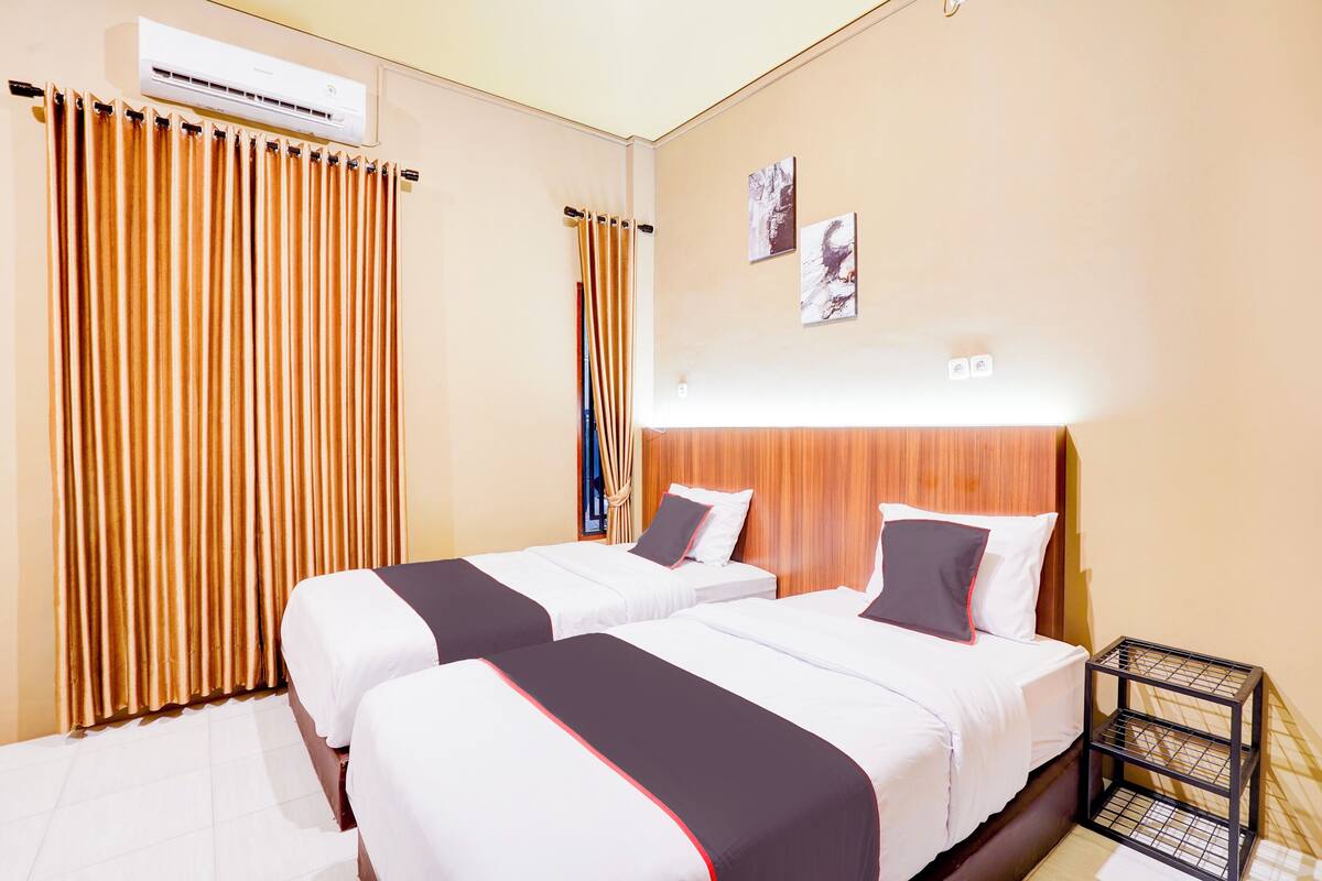 Quarto de hotel com duas camas, uma cabeceira de madeira, um ar condicionado e uma mesa de cabeceira.