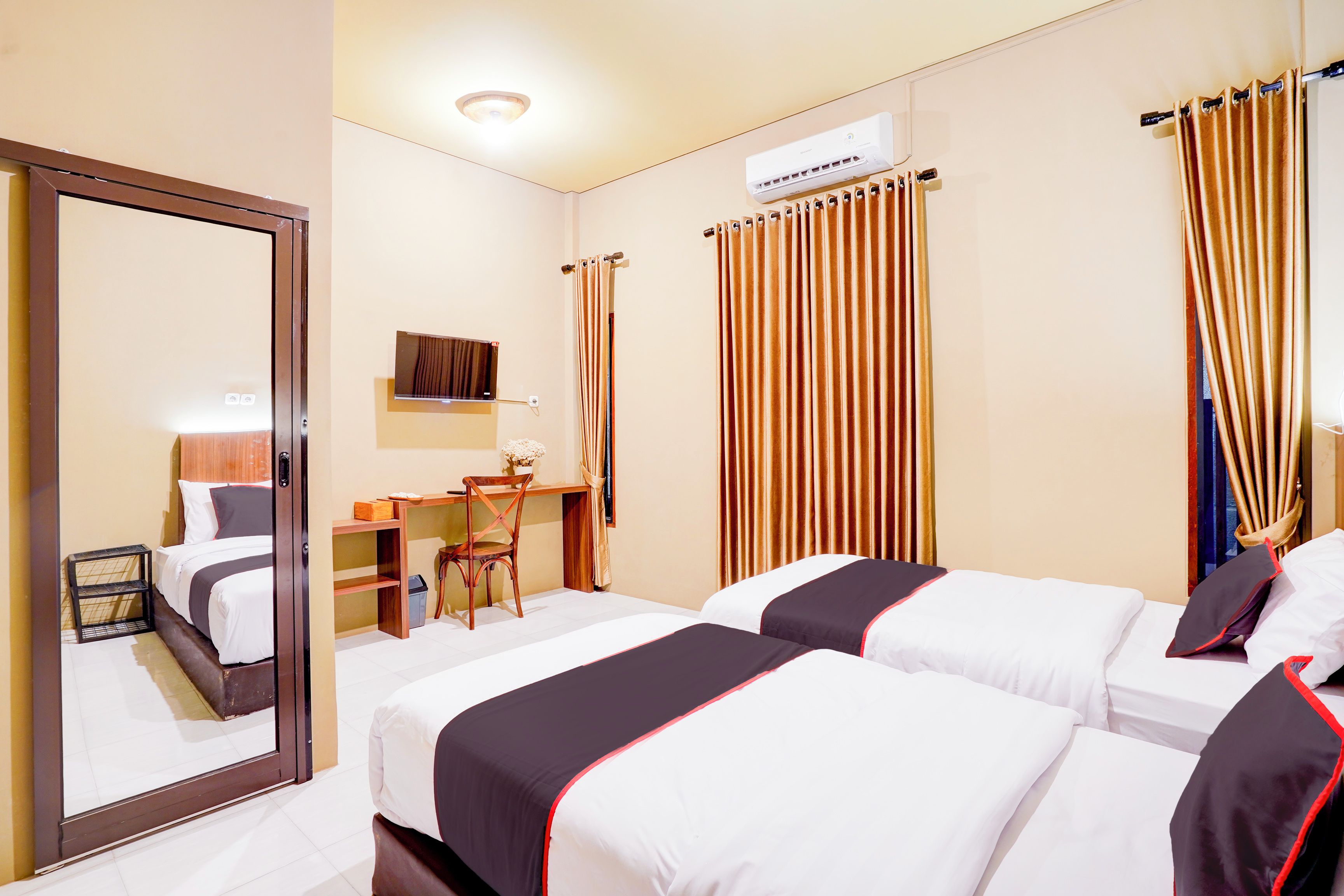 A hotel room with two beds, a desk, a chair, and a mirror.