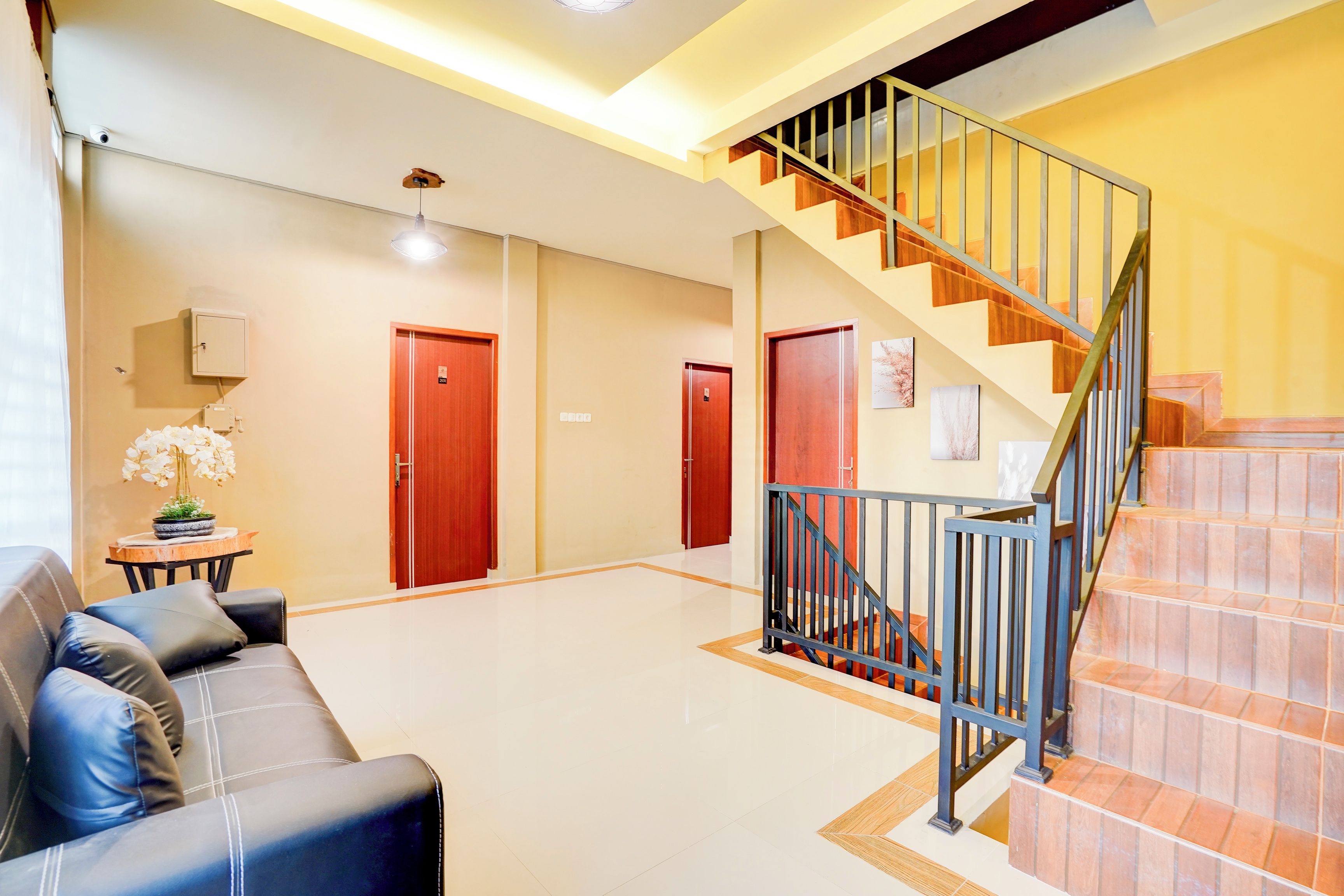 A spacious lobby with a black leather sofa, a staircase with a metal railing, and a tiled floor.
