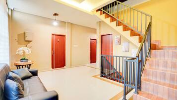 A spacious lobby with a black leather sofa, a staircase with a metal railing, and a tiled floor.