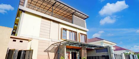 A modern two-story house with a covered entrance, a balcony, and a gated driveway.