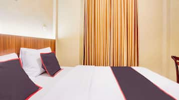 Una habitación de hotel con una cama bien hecha, cabecera de madera y cortina a rayas verticales.