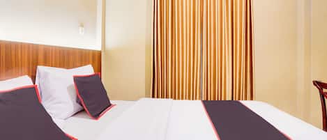 Una habitación de hotel con una cama bien hecha, cabecera de madera y cortina a rayas verticales.