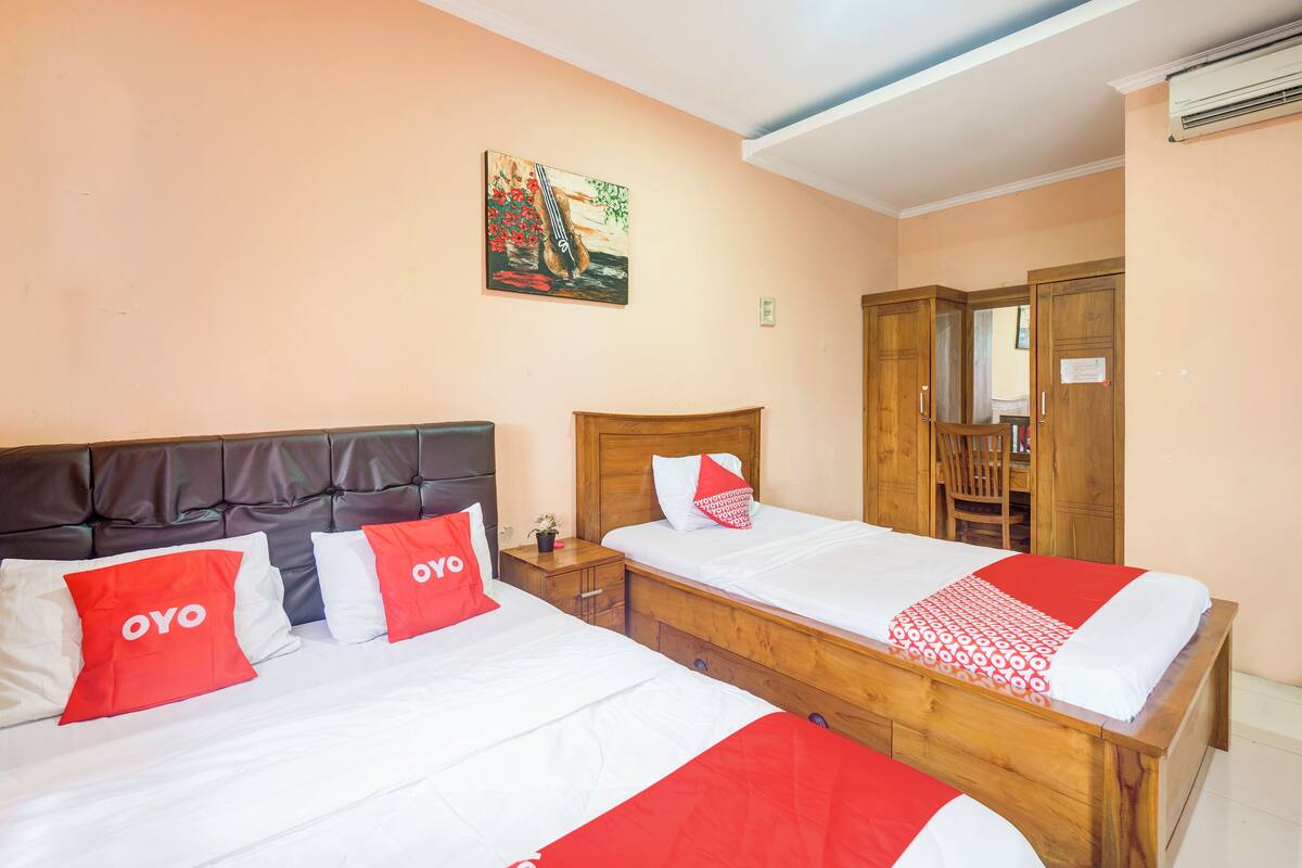 A hotel room with two beds, each with red and white bedding, a wooden headboard, and a painting on the wall.