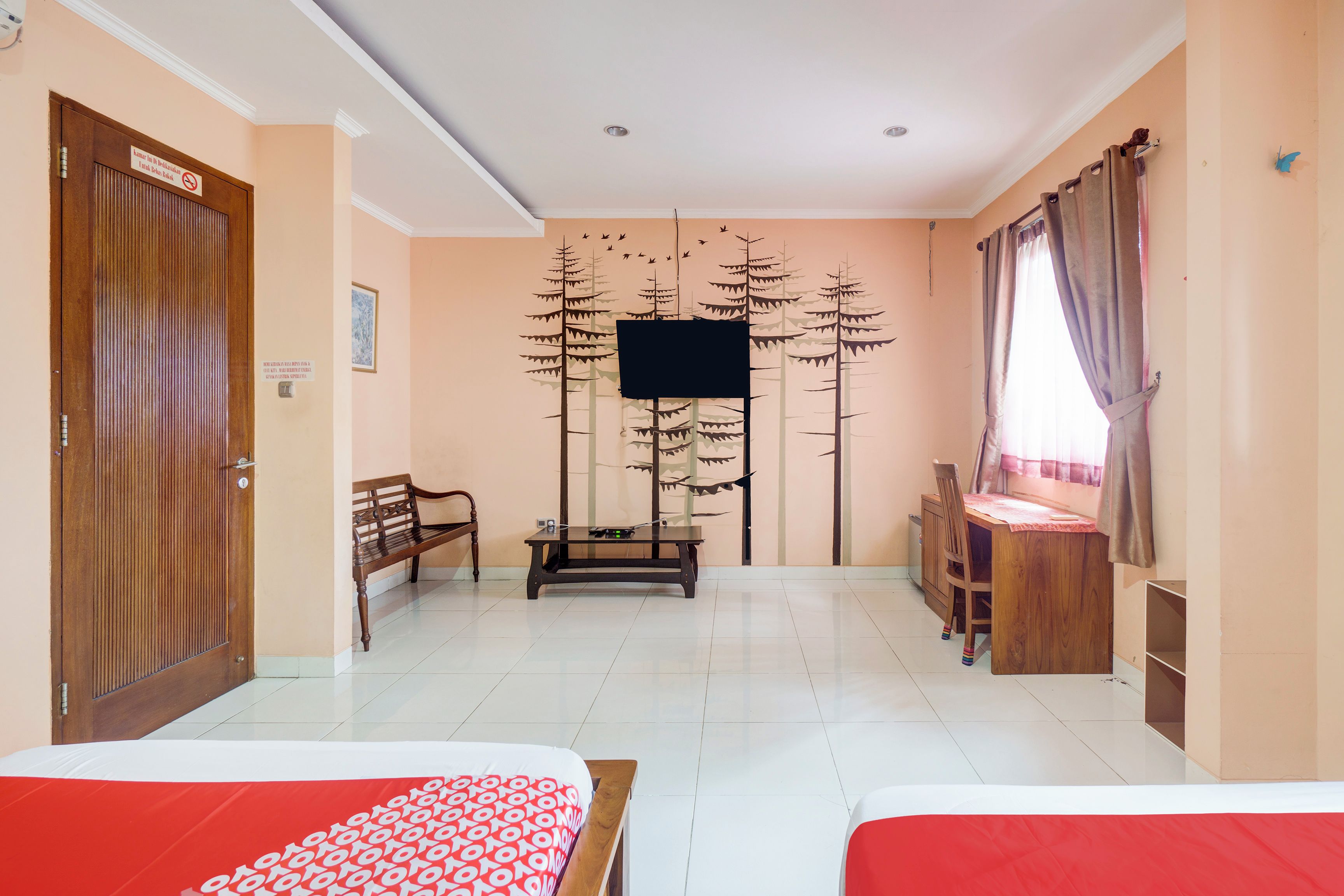 Habitación de hotel con dos camas, un escritorio de madera, un banco, un televisor montado en la pared y una ventana con cortinas.