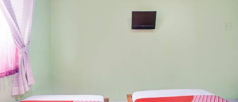 Una stanza con due letti, una televisione appesa al muro e una tenda a sinistra.