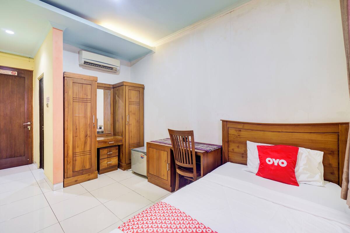 A bedroom with a bed, a desk, a chair, wooden wardrobes, and an air conditioner.