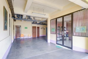 Um corredor amplo com piso de azulejos, portas de madeira e uma porta de vidro que dá para um espaço com sapatos expostos.