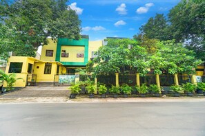 A multi-story building with a green and yellow facade, surrounded by potted plants and trees. - Hotel O Tebet Near Tebet Station (Jakarta)