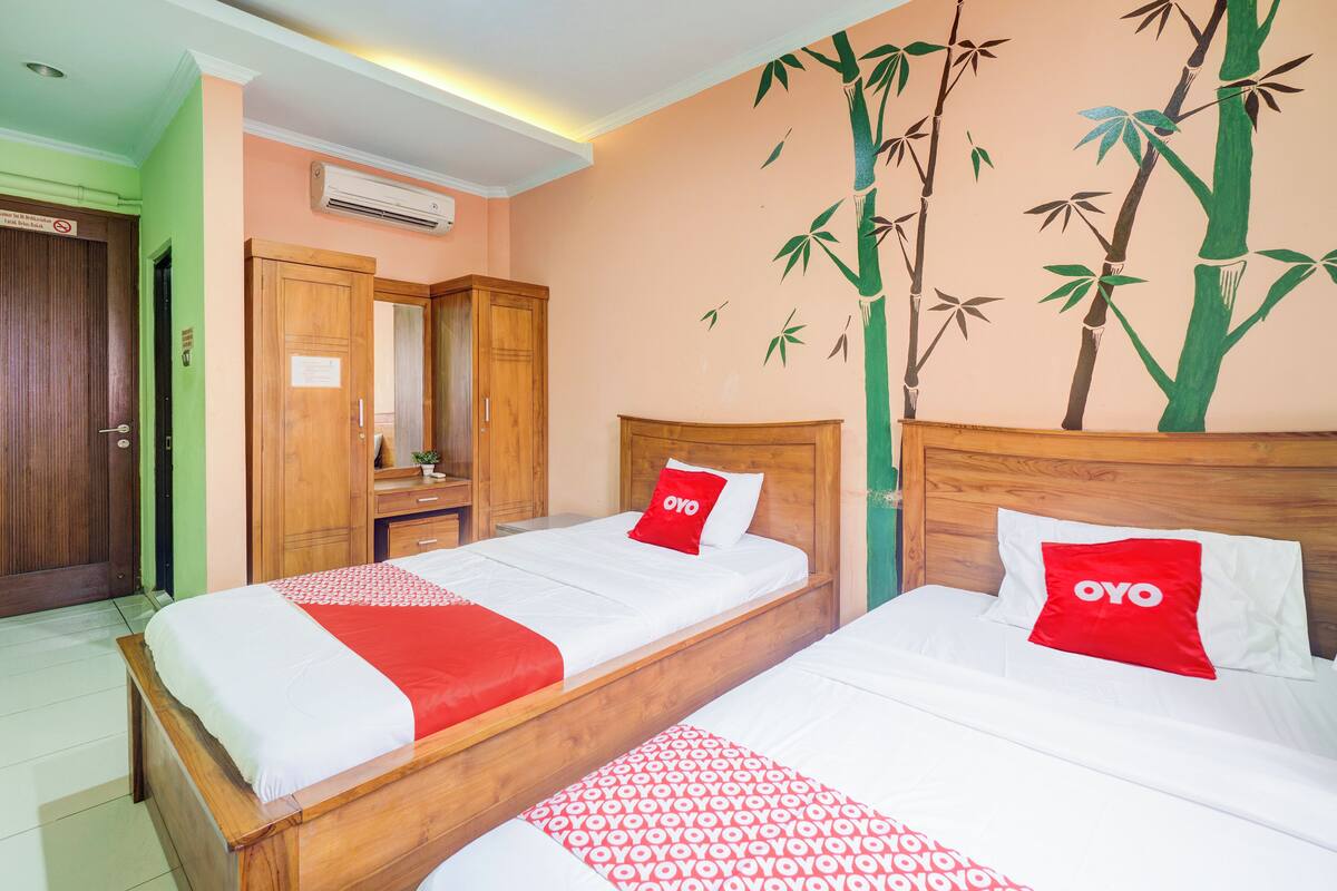 A hotel room with two beds, a wooden wardrobe, a mirror, and a wall mural.