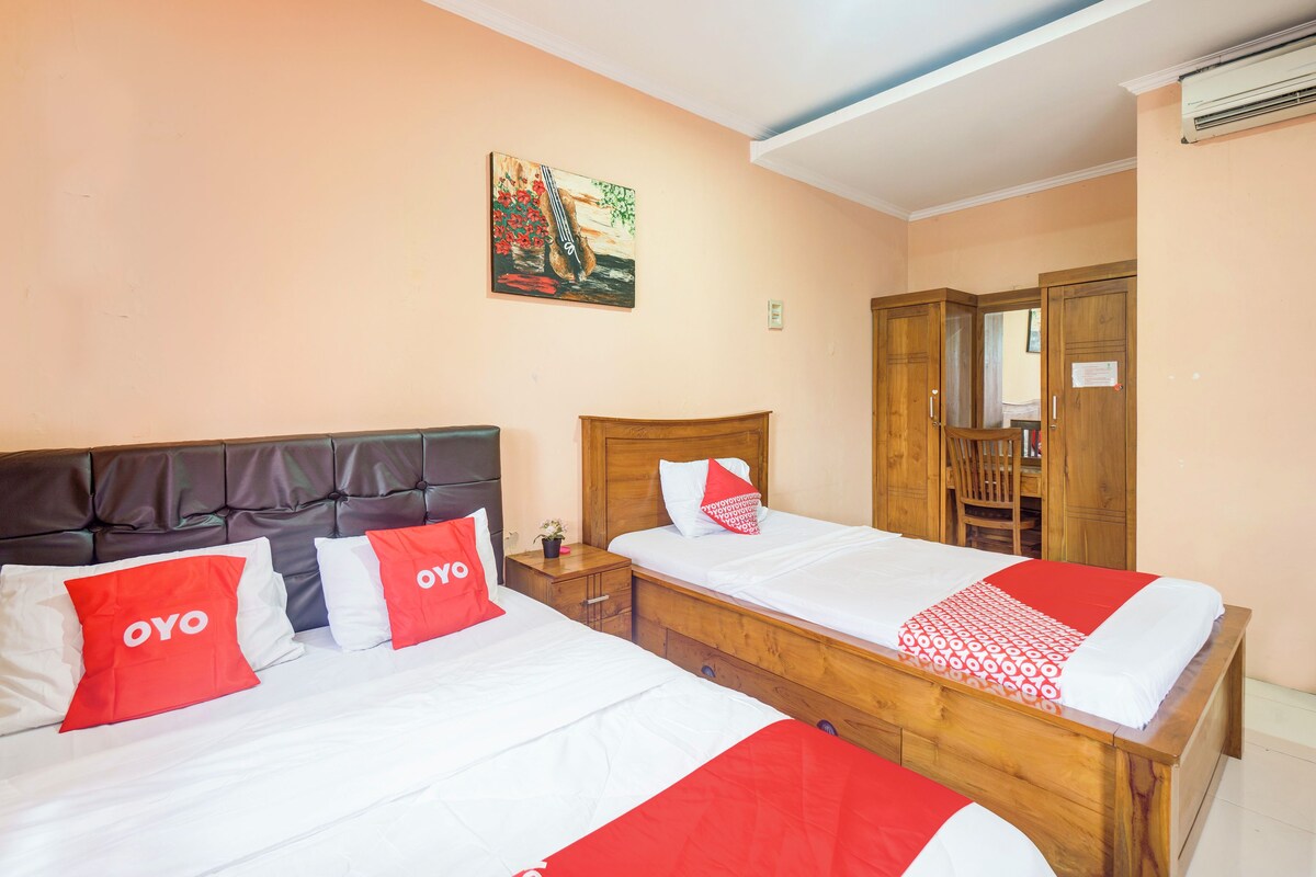 Quarto de hotel com duas camas, cada uma com roupa de cama vermelha e branca, uma cabeceira de madeira e um quadro na parede.