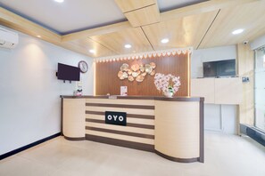 Uma receção com uma placa a indicar "OYO", uma televisão montada e um painel decorativo na parede.