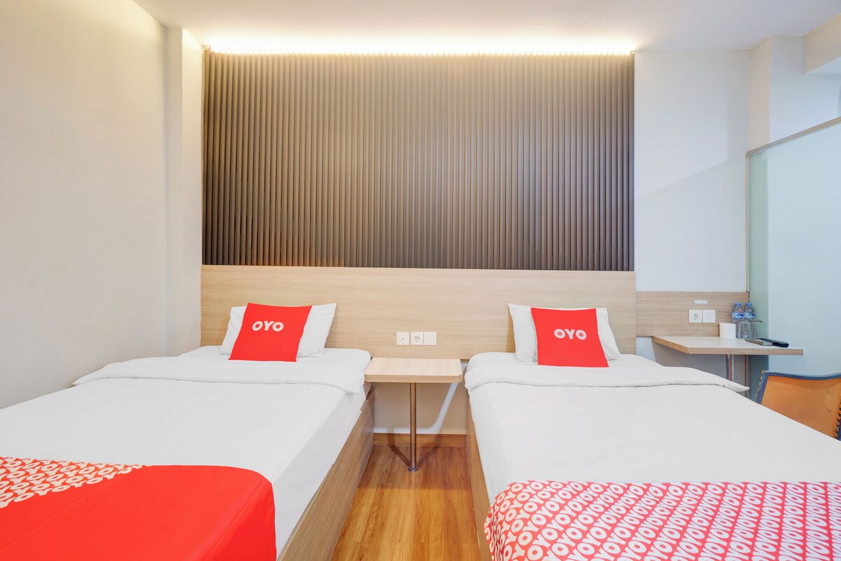 Habitación de hotel con dos camas, cada una con un almohadón rojo, una mesita y un espejo.
