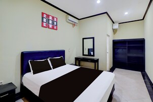 A hotel room with a bed, bedside table, mirror, wardrobe, and wall-mounted air conditioning unit.