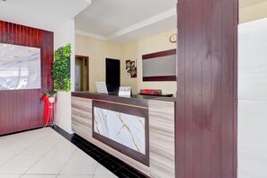 A reception area with a marble-patterned counter, a potted plant, a laptop, and a clock on the wall. - Collection O Near Bali Royal Hospital Renon (Denpasar)
