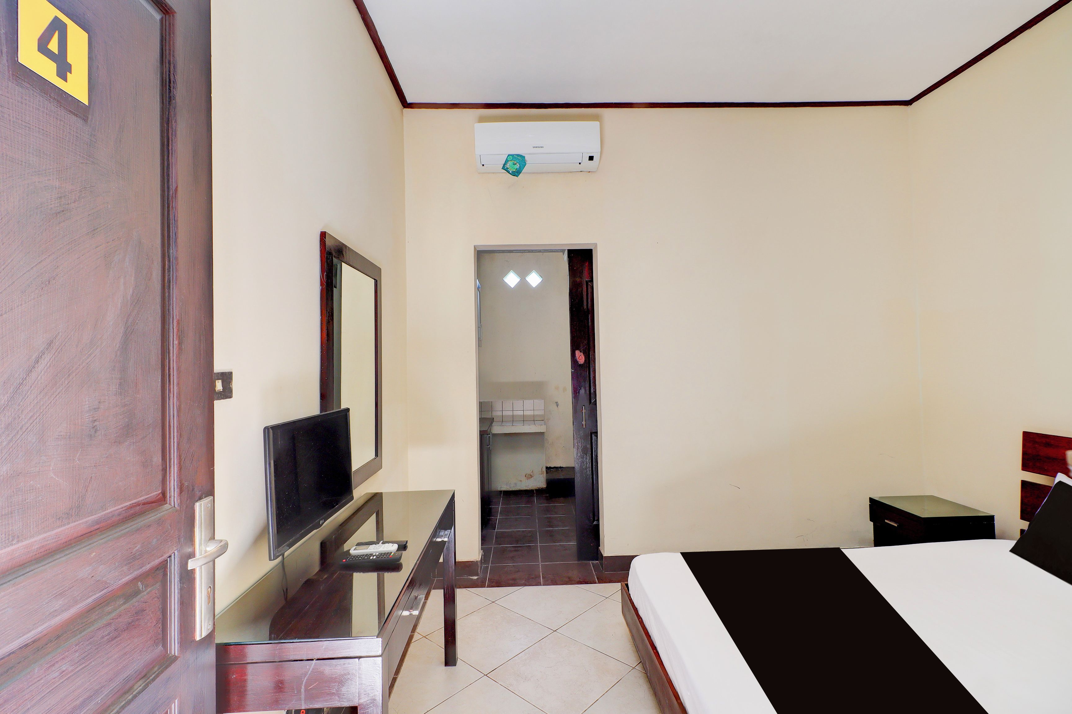 Une chambre d’hôtel comprenant un lit, un bureau avec une télévision, une armoire et une salle de bain visible à travers une porte ouverte.