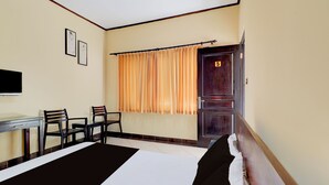 A hotel room with a bed, a desk, chairs, a window with curtains, and a door with a number. - Collection O Near Bali Royal Hospital Renon (Denpasar)
