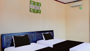 A room with two beds, a blue headboard, and a wall-mounted air conditioner. - Collection O Near Bali Royal Hospital Renon (Denpasar)