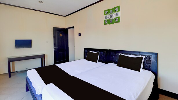 A hotel room with a large bed, a desk, and a door. - Collection O Near Bali Royal Hospital Renon (Denpasar)