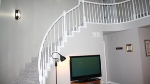 A staircase with white railings, a television on a stand, and wall-mounted lights. - Cozy Court House near Flower Mound and Lewisville (Flower Mound)