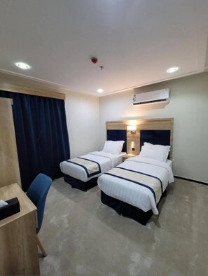 A hotel room with two beds, a desk, a chair, an air conditioning unit, and a ceiling light. - Gardenia Park Al Zaharaa (Jeddah)