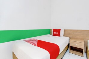 Una cama individual con una colcha roja y blanca, un cojín a juego y una mesita de noche de madera con un cajón.