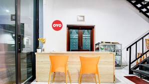 A reception area with a wooden counter, two orange chairs, a vase with flowers, and a staircase to the right. - Collection O Jalan Slamet Riyadi Kampung Batik K (Surakarta)