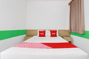 A neatly made bed with a red and white patterned blanket, two red pillows with "OYO" text, a wooden headboard, and a wooden nightstand with a drawer. - Collection O Jalan Slamet Riyadi Kampung Batik K (Surakarta)