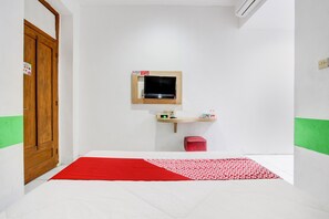 A room with a bed, a wooden wardrobe, a small sink, a mirror, and a red and white patterned rug. - Collection O Jalan Slamet Riyadi Kampung Batik K (Surakarta)