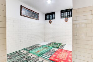 Una habitación con paredes de azulejos blancos, un texto religioso enmarcado y una esterilla de oración.