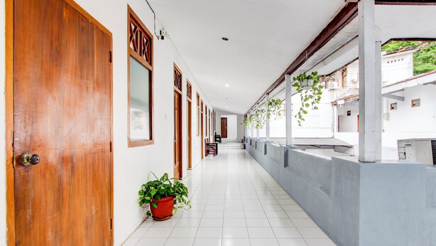 A corridor with wooden doors, potted plants, and a tiled floor. - Collection O Jalan Slamet Riyadi Kampung Batik K (Surakarta)