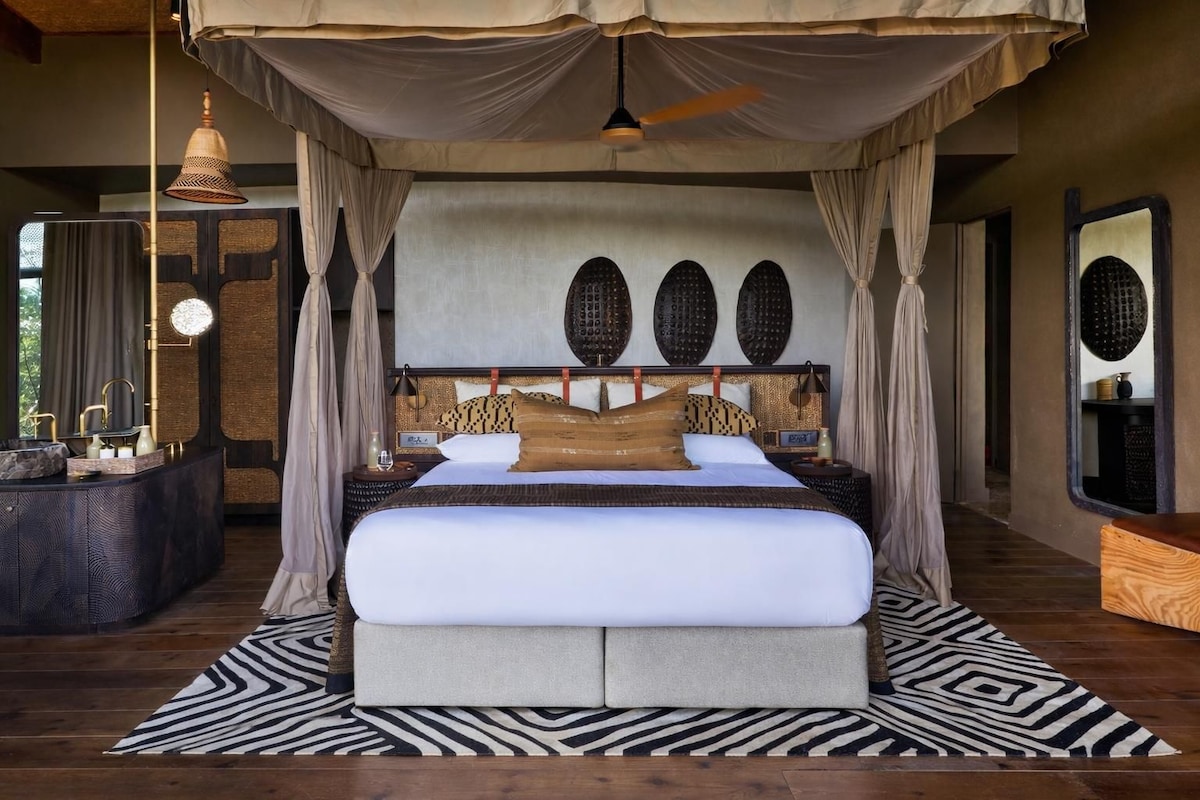 A large bed with a canopy, a round wall clock, and a large mirror.