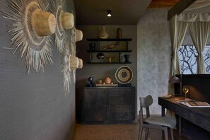 A room with a dark wooden desk, a chair, a shelf with decorative items, and a wall with a textured pattern. - Bupenyu Luxury Boutique Lodge (Matabeleland North)