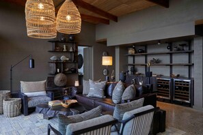 A modern living room with a sofa, armchairs, a coffee table, wicker baskets, a floor lamp, and a wine rack. - Bupenyu Luxury Boutique Lodge (Matabeleland North)