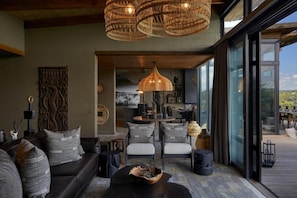 A modern living room with a sofa, chairs, a coffee table, and a large window. - Bupenyu Luxury Boutique Lodge (Matabeleland North)