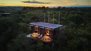Uma cabana moderna e elevada, com telhado plano, rodeada por uma floresta densa.