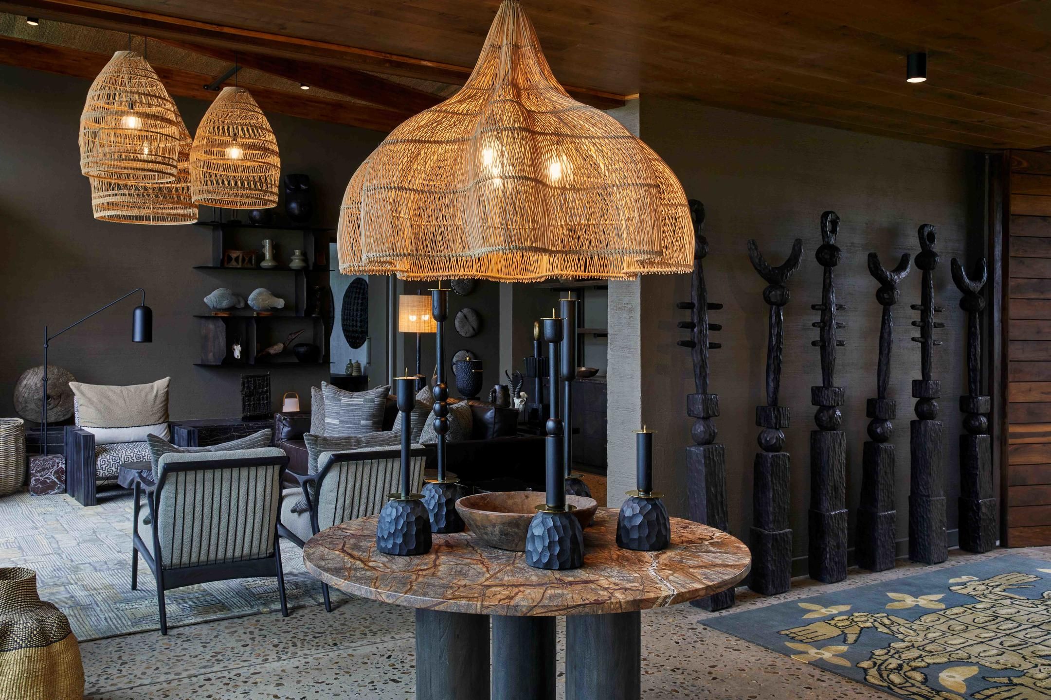 Una habitación con lámparas colgantes de mimbre, una mesa redonda con jarrones y una pared decorada con objetos metálicos.