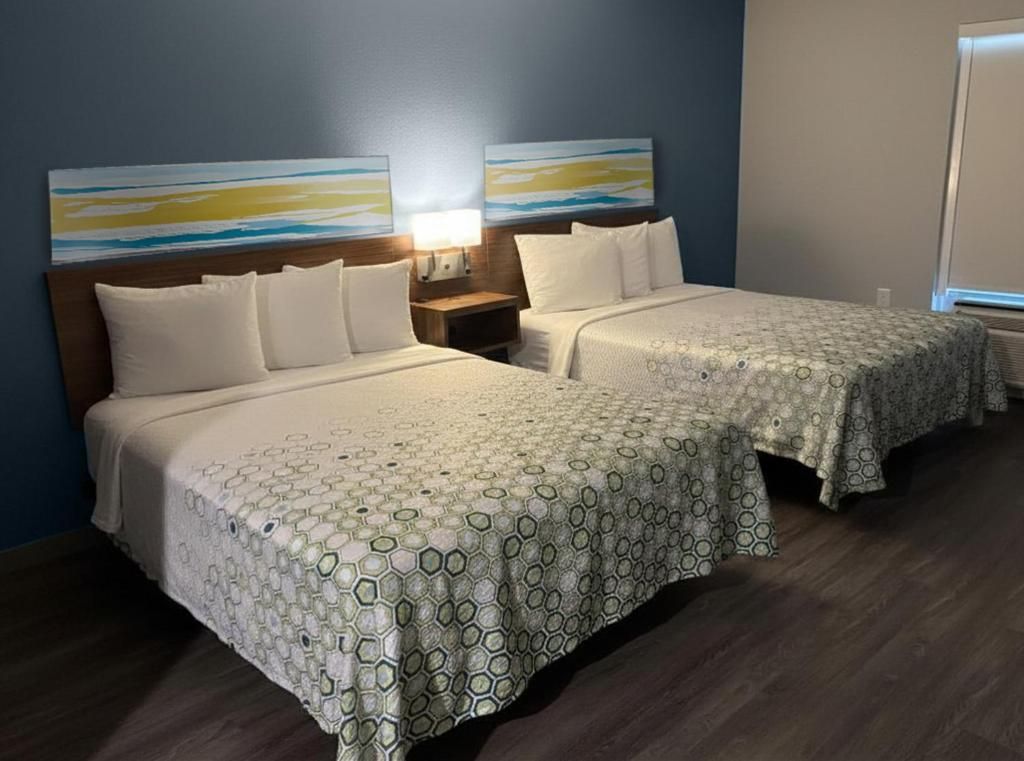 Une chambre d’hôtel avec deux lits, une table de chevet, une lampe et des œuvres d’art abstraites accrochées au mur.
