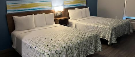 A hotel room with two beds, a nightstand, a lamp, and abstract wall art.