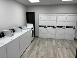 Un cuarto de lavandería con varias lavadoras y secadoras, piso de madera y pared blanca lisa.