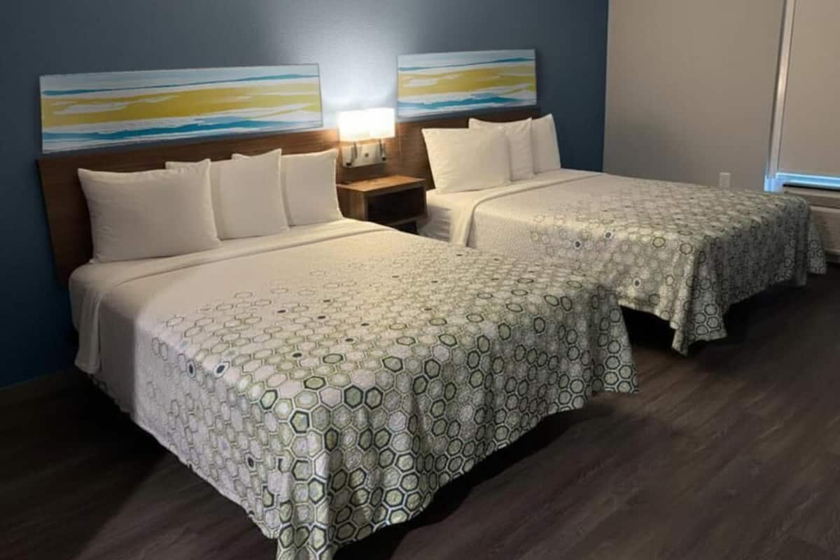 Habitación de hotel con dos camas, una mesita de noche, una lámpara y arte abstracto en la pared.